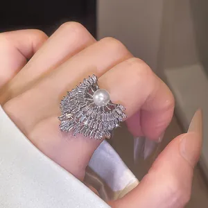 Gros plan d'une bague ouverte étincelante en zircon et perle au design géométrique.