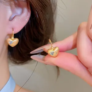 Close-up of golden heart-shaped ear buckles with zircon inlay and matte finish