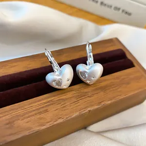 Detail shot of matte silver heart earrings with sparkling cubic zirconia on wood.