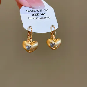 Close-up detail of matte gold heart earrings with sparkling heart-shaped zircon inlay