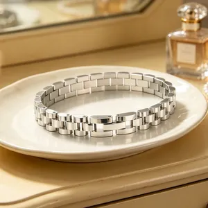Close-up detail of a stainless steel watch strap style link bracelet on a cream ceramic plate.