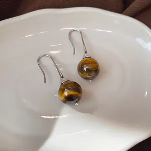 Detailed view of vintage tiger eye stone drop earrings with silver hooks on a white dish