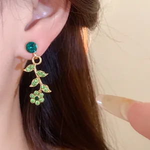 Close-up detail of elegant gold-toned flower drop earrings featuring green rhinestones