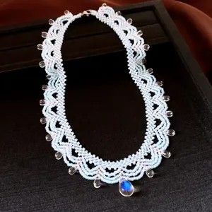 Gros plan d'un collier en dentelle de perles bleu clair avec pendentif goutte iridescent.