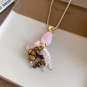 Detailopname van een boho-stijl kwastjesketting met roze steen en tijgeroog kralen