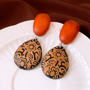 Gros plan de boucles d'oreilles en bois en forme de goutte avec motif floral noir