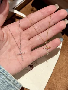 Gros plan de colliers croix en or et argent avec zircons marquise sur la main.