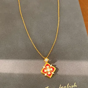Primo piano di una collana vintage placcata oro 24K con fiore in smalto rosso e zirconi