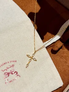 Détail d'un collier français avec pendentif croix en zircon irrégulier sur chaîne dorée.