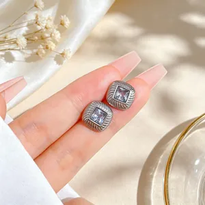 Close-up of minimalist titanium steel square zircon stud earrings held by hand.