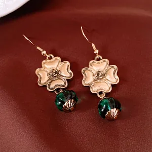 Nahaufnahme von Vintage-Goldblumenohrringen mit eleganten grünen Glaslaternenperlen