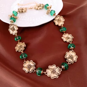 Nahaufnahme einer Retro-Halskette mit Goldblumen und grünen Glasperlen auf brauner Seide