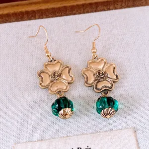 Makroansicht goldener Blumenohrringe mit smaragdgrünen Glasperlen auf Leinenhintergrund