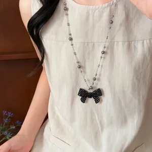 Lange ketting met grijze parels en een zwarte polkadot strikhanger op linnen jurk