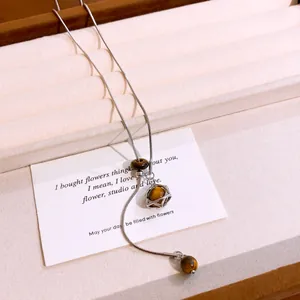 Close-up of tiger eye stone necklace with a geometric star cage pendant detail.