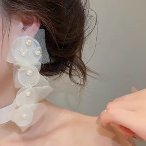 Detaillierte Nahaufnahme eines langen weißen Chiffon- und Perlenohrrings an einem Ohr