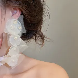 Nahaufnahme von eleganten weißen Chiffon-Ohrringen mit Perlenakzenten am Modell