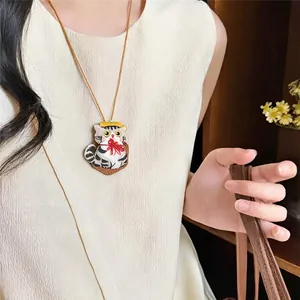 Close-up detail of a cute embroidered grey striped cat pendant necklace on a beige dress