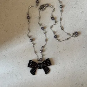 Detailweergave van een parelketting met een zwart gestipte strik hanger van acryl.