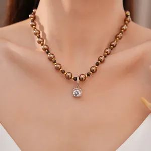 Detail van tijgeroog parelketting met vierkante zirkoon hanger gedragen door een model.