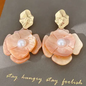 Close-up of peach acrylic flower stud earrings with pearl center and gold metal details