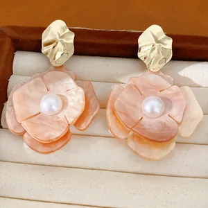 Close-up of elegant acrylic flower earrings with faux pearls and gold-plated details