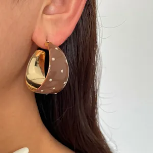 Detailansicht eines braunen Emaille-C-Ohrrings mit weißen Punkten auf dem Ohr
