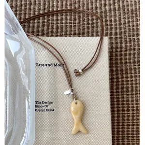 Detail van een minimalistische stenen vis hanger ketting aan een bruin leren koord