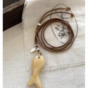 Detail van een minimalistische vishanger van steen aan een bruin leren koord ketting