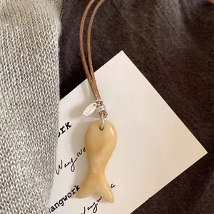 Close-up van een minimalistische ketting met visvormige stenen hanger en leren koord