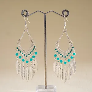 Vue détaillée de boucles d'oreilles bohèmes argentées avec perles turquoise et plumes.