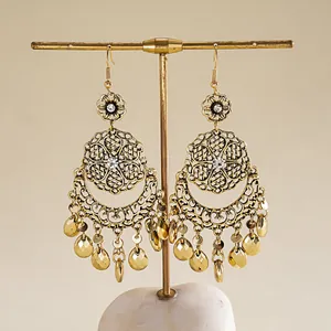 Boucles d'oreilles pendantes dorées avec découpes géométriques sur un support à bijoux.