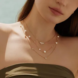 Primer plano de un elegante collar de acero de titanio dorado con perlas y circonitas.