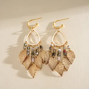 Détail de boucles d'oreilles dorées à pampilles de feuilles et perles en résine