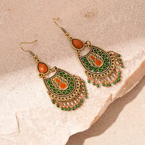Détail de boucles d'oreilles bohèmes avec incrustations en résine et franges perlées.