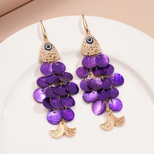 Détail de boucles d'oreilles élégantes en forme de poisson aux écailles violettes.