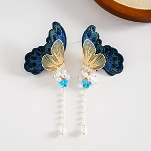 Détail de boucles d'oreilles papillon avec broderie bleue et longs glands en perles