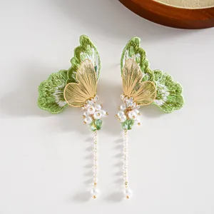 Vue détaillée de boucles d'oreilles papillon avec broderie verte et longs glands de perles.