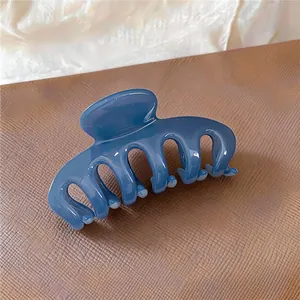 Close-up of a glossy blue acrylic shark hair claw clip on a textured surface.