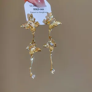 Detailweergave van gouden vlinder oorbellen met kristallen en zilveren naalden.