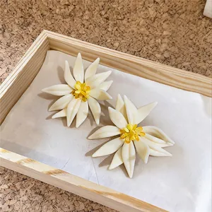 Vue détaillée d'élégantes boucles d'oreilles fleurs en cristal blanc crème et jaune dans un plateau.