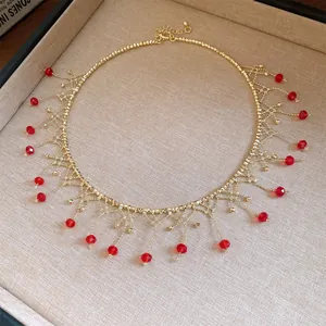 Detail view of a gold choker necklace with elegant red beaded fringe tassels and gold link.