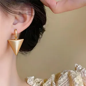 Detail shot of minimalist matte gold triangle pendant hoop earrings worn by a model