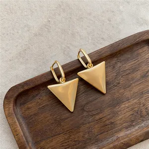 Detailed view of gold-tone matte triangle pendant hoop earrings on a wooden tray.