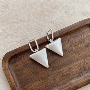 Close-up of elegant triangular pendant earrings with pearlescent finish on wooden tray