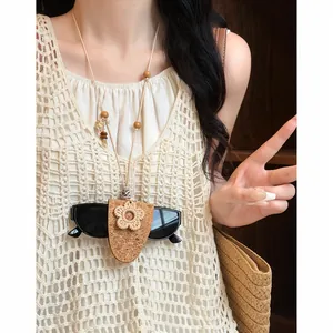 Dettaglio di una collana porta occhiali boho con fiore su modella con gilet in maglia crema