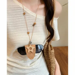 Dettaglio della clip in legno a forma di stella su una collana in pelle che tiene gli occhiali.
