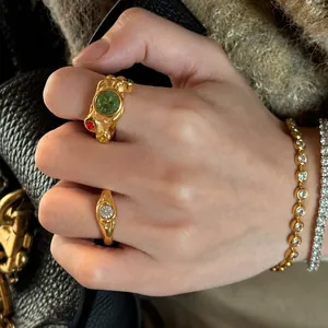 Détail en gros plan d'une bague dorée irrégulière avec pierres colorées sur la main.
