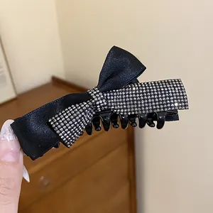 Vue détaillée d'une pince à cheveux en satin noir avec nœud et strass brillants
