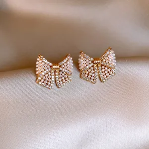 Nahaufnahme eleganter goldener Schleifenohrringe mit Kristallen und weißen Perlen